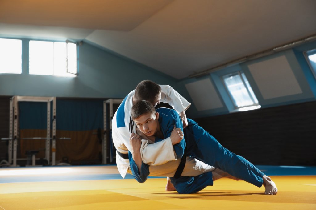 Two young judo fighters in kimono training martial arts in the gym with expression, in action and